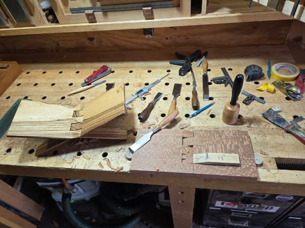A workbench mid-job: chisels, mallet, plane, and dovetail jig in a dust of shavings.